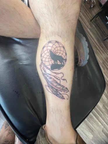 Dreamcatcher tattoo with a wolf silhouette on calf.