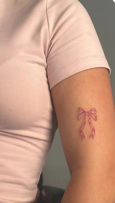 Small pink bow tattoo on upper arm.