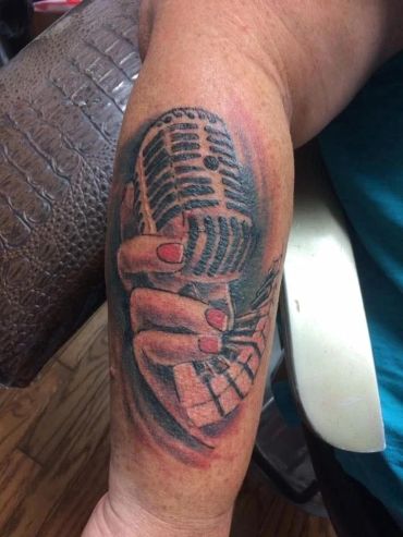 Hand holding a vintage microphone tattoo.