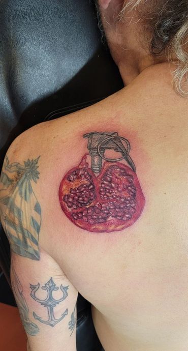 Red pomegranate fruit tattoo on a shoulder.
