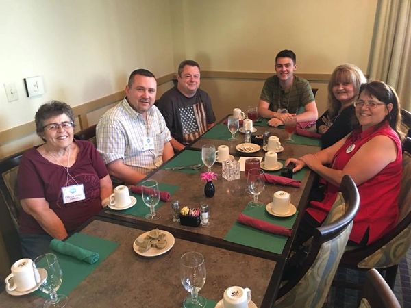 A group of six people seated around a dining table, smiling.