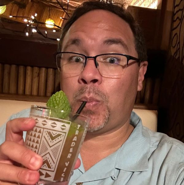 Man sipping a mint garnish drink through a straw in a cozy setting.