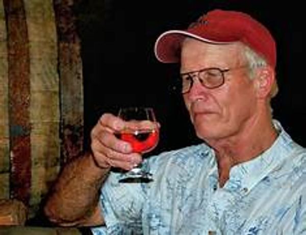 Older man in red cap holding a glass of red drink.
