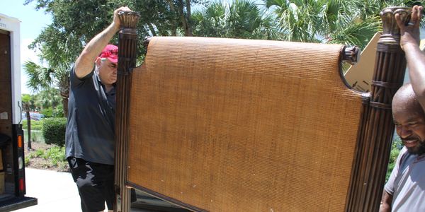 Two men moving a large wooden headboard outside.