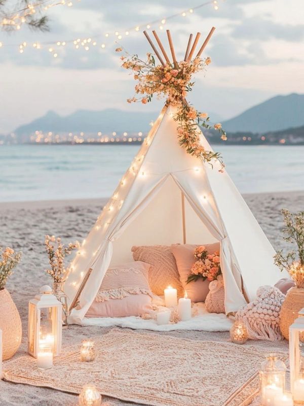 Cozy beach tent with pillows, candles, and fairy lights at sunset.