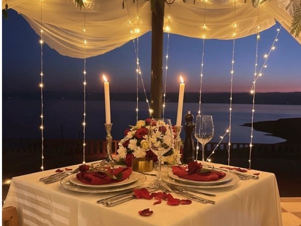 Romantic candlelit dinner setup by the water at dusk with string lights.