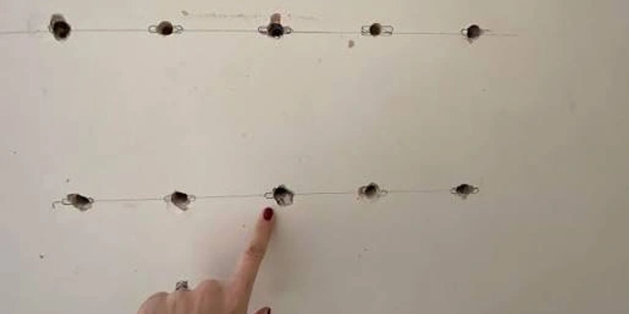 Finger pointing at holes on a wall connected with wires.
