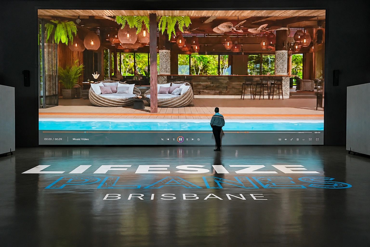 Person watching a large screen showing a poolside scene at Lifesize Planes Brisbane.