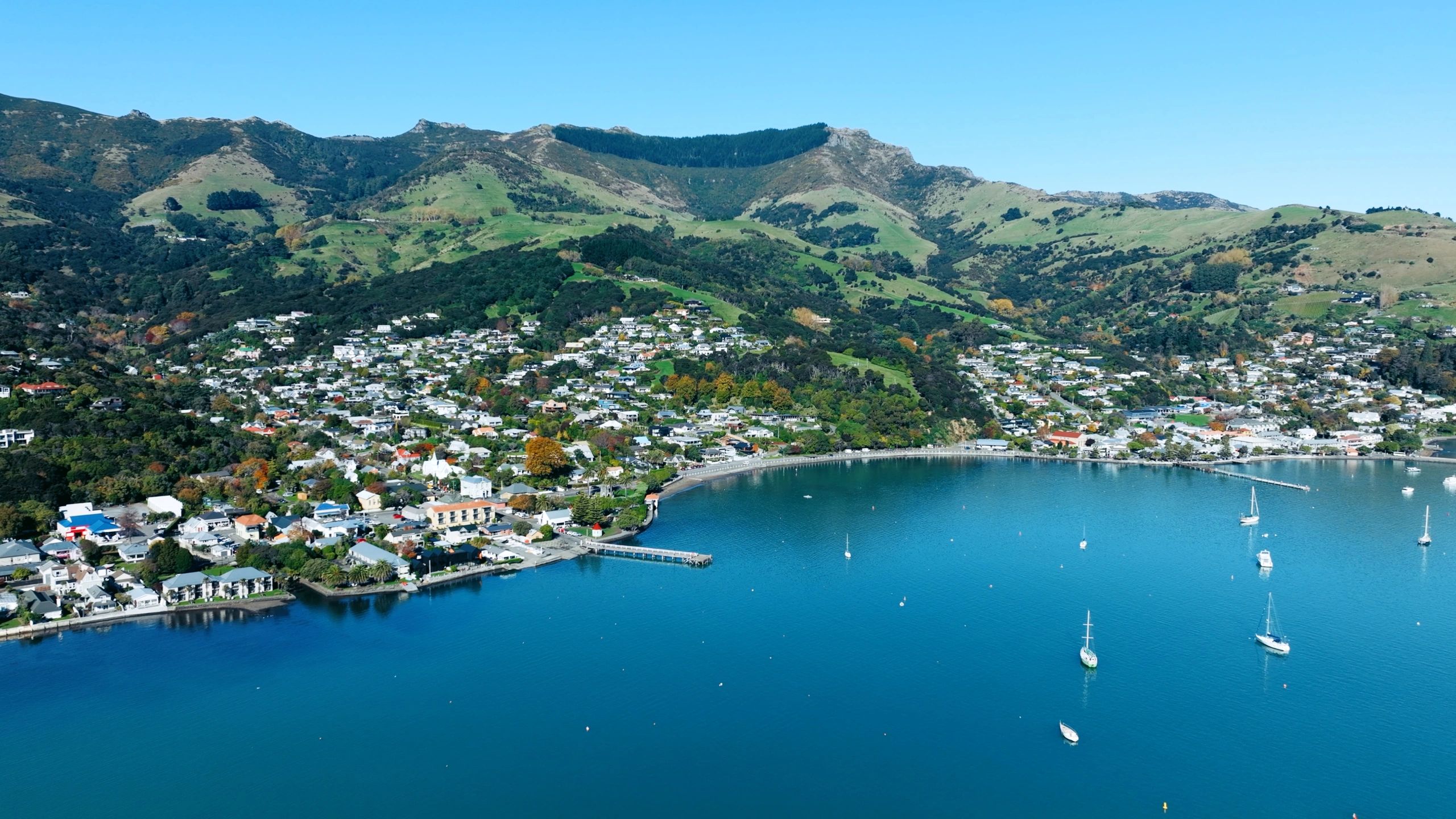 Coastal town nestled between green hills and blue waters with boats sailing.