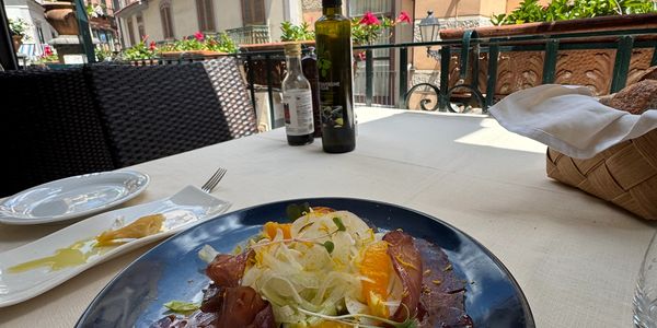 A fresh salad with orange slices on a blue plate at an outdoor restaurant.