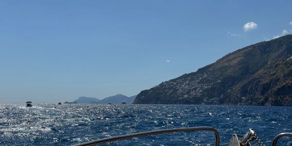 View from a boat on the sparkling sea near a rocky coastline under a clear blue sky.