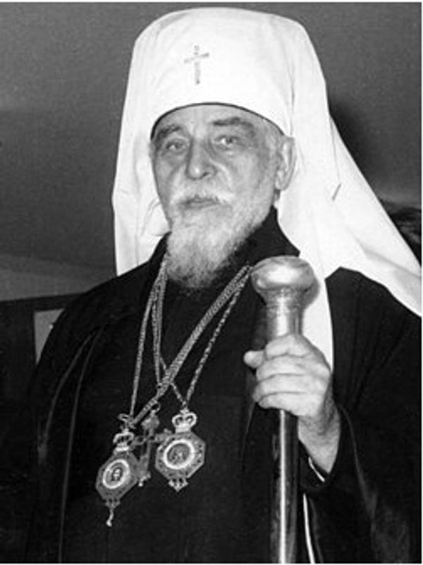 An elderly religious leader in traditional attire holding a staff.
