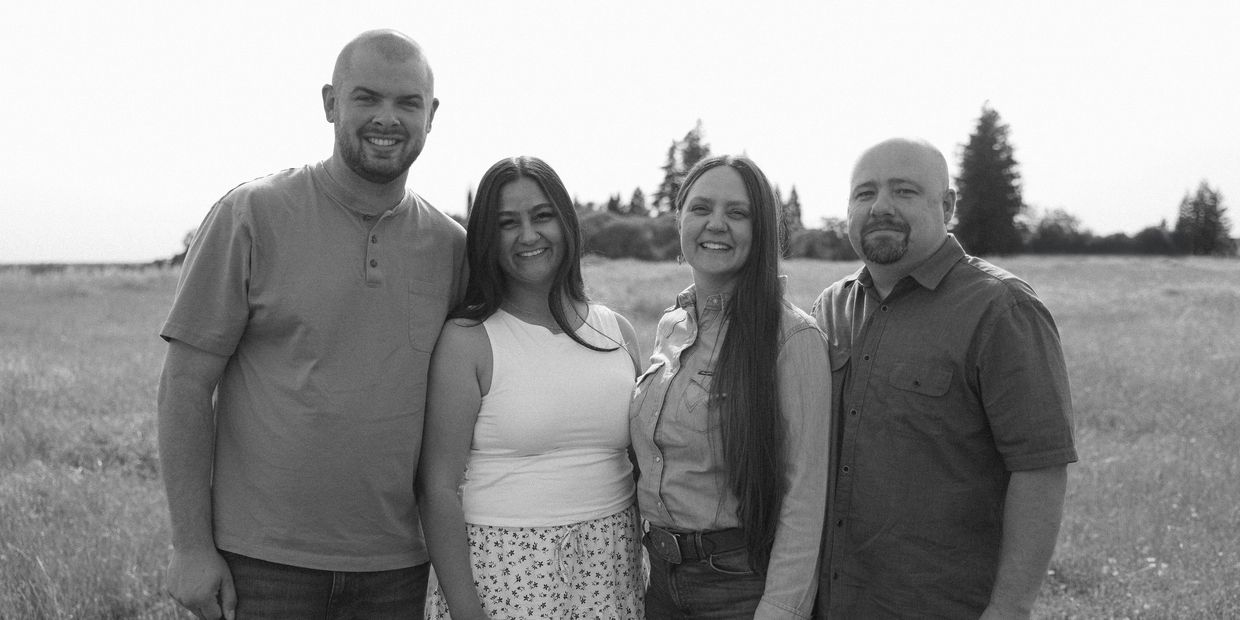 Four adults smiling together in a field, black and white photo.