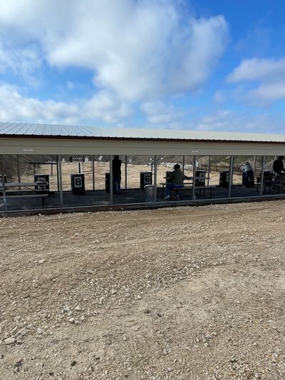 Outdoor shooting range with people practicing under a covered area.