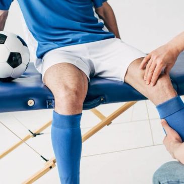 Soccer player receiving knee treatment while sitting on a medical table.