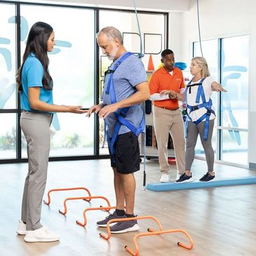 Therapists assist patients with balance and mobility exercises using harness support.