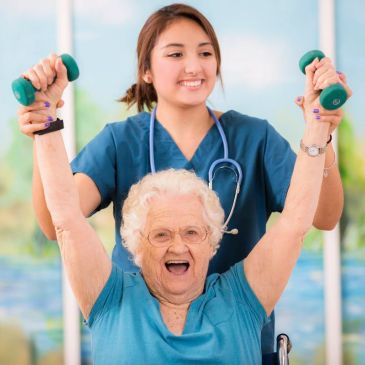 Elderly woman exercising with assistance from a smiling healthcare worker.