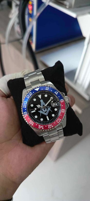 Hand holding a silver wristwatch with a blue and red bezel and a black dial.