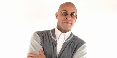 Confident man in glasses and cardigan posing with arms crossed.
