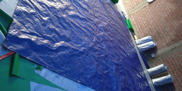 Large blue tarp spread out with rolls of similar material nearby in a workshop.