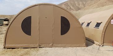 Large brown military-style tent with semi-circular windows in a desert setting.