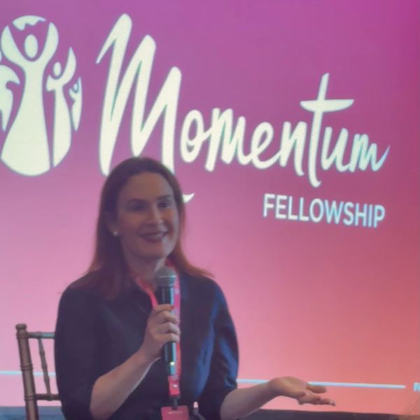 A woman speaking at Momentum Fellowship event with a microphone.