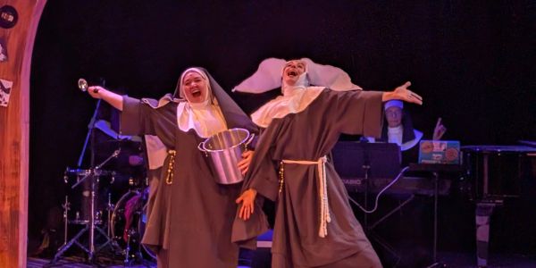 Two nuns performing joyfully on stage with a microphone and bucket.