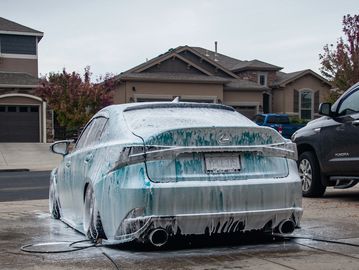A car covered in soap suds during a wash in a driveway.