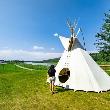 A woman walking towards a white teepee on a sunny day near a lake.