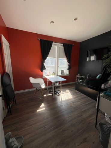 A cozy room with red and black walls, a small white table, and sunlight streaming through windows.