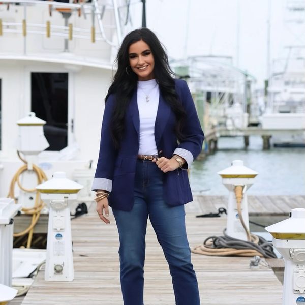 Smiling woman in navy blazer and jeans on a dock.