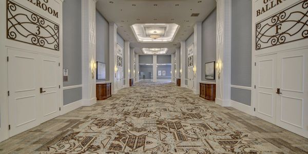 Elegant hotel corridor leading to a ballroom with intricate carpet and soft lighting.