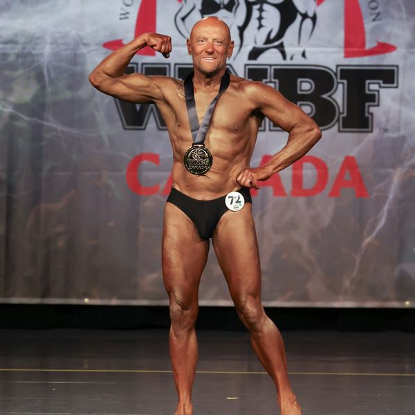 Bodybuilder posing proudly on stage with a medal at a WNBF Canada competition.