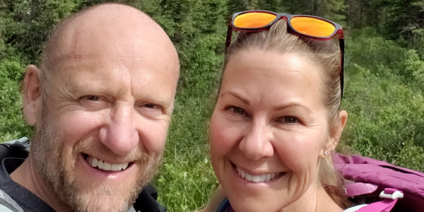 Smiling couple hiking in a lush forest with mountains in the background.