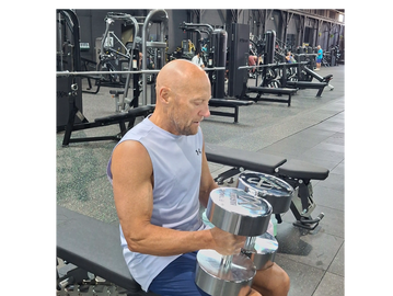 Man lifting heavy dumbbells while seated on a gym bench.