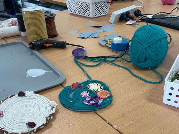 Crafting project with yarn, glue gun, and decorative flowers on a table.