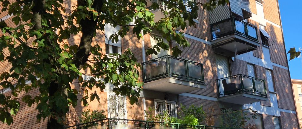 Palazzo con balconi e alberi davanti in una giornata soleggiata.
