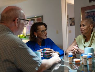 Three adults talking at a table with medication bottles.