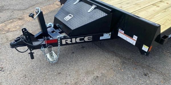 Close-up of a Rice brand flatbed trailer hitch and toolbox on pavement.