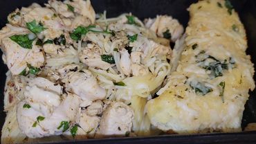 Cooked chicken with herbs and a cheesy side dish in a pan.
