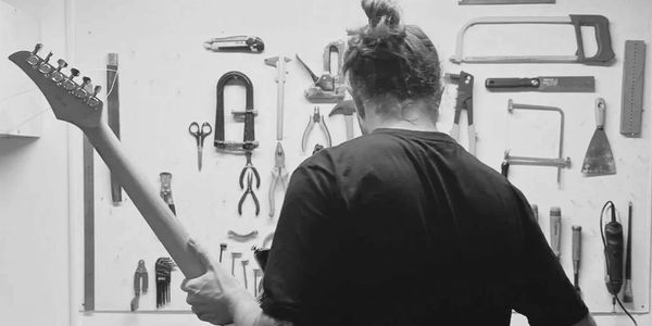 Luthier de costas segurando braço de guitarra. Zafímera