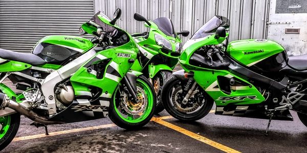 Three green Kawasaki motorcycles parked side by side in an industrial area.