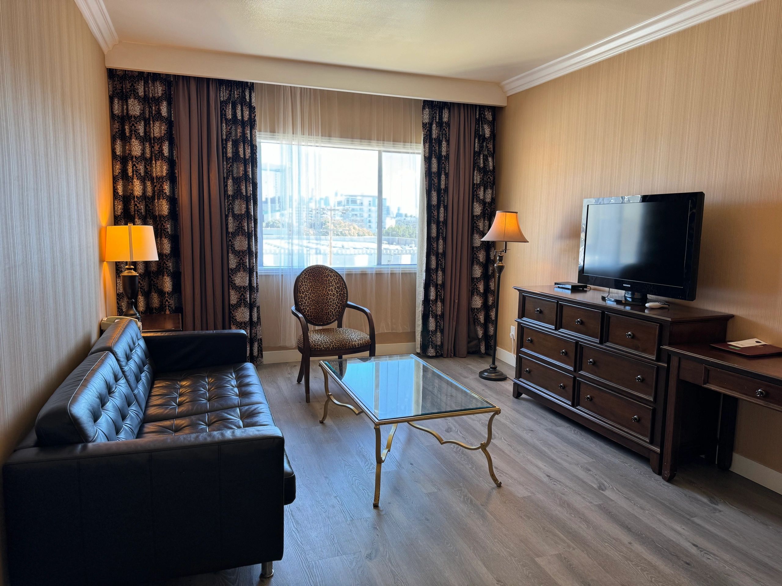 A hotel living room with a sofa, chair, coffee table, TV, and dresser.
