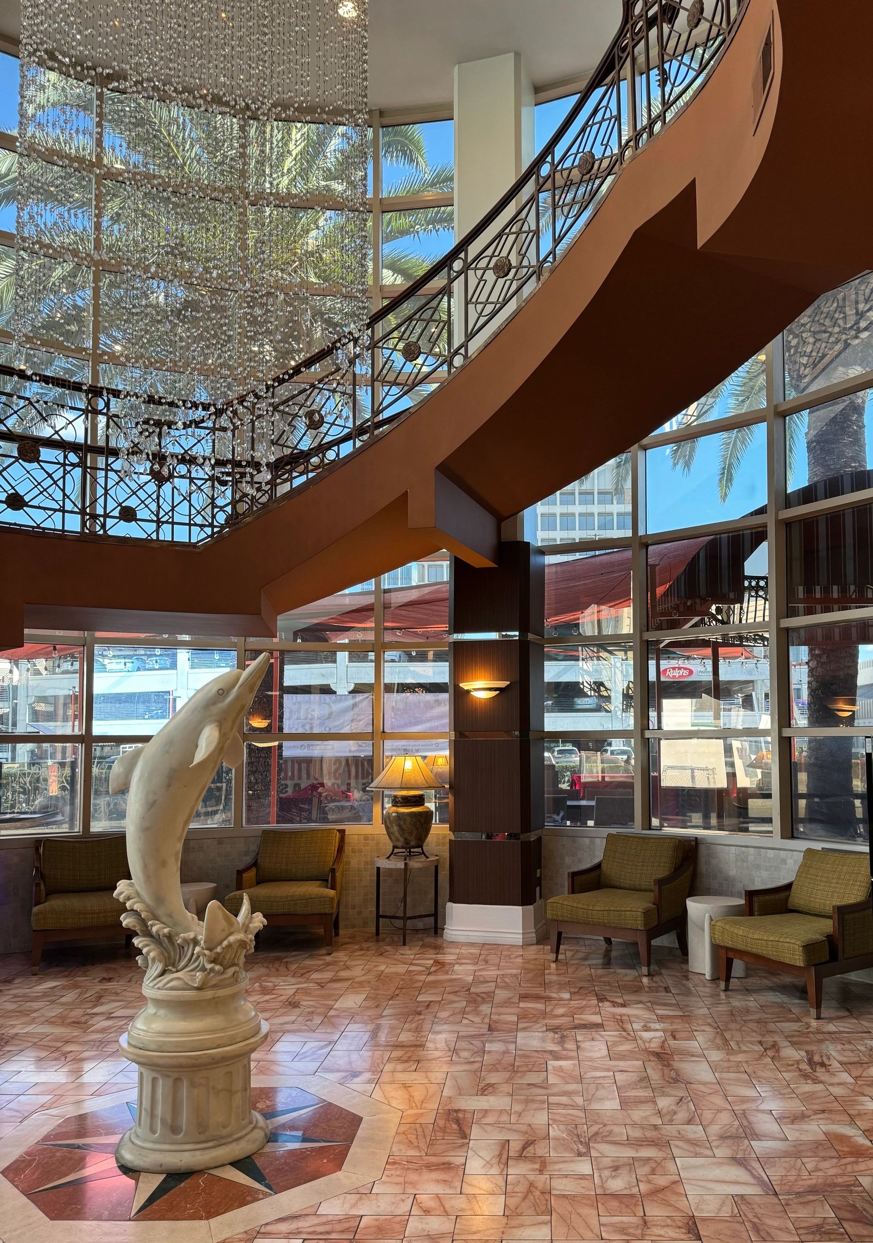 A spacious lobby with a curved staircase, a large statue, and a chandelier.
