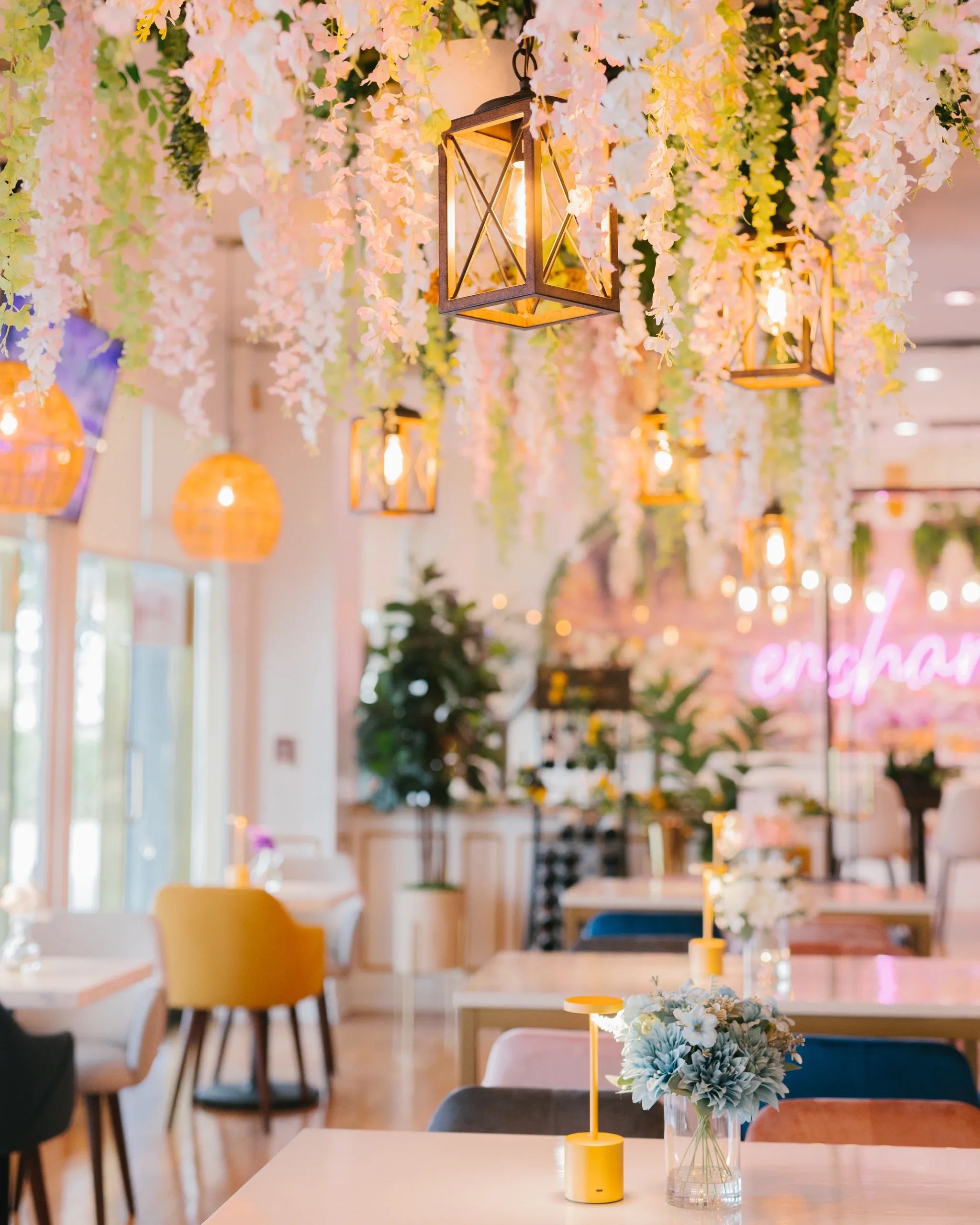 A brightly lit dining area with tables, chairs, and decorative flowers and lanterns.