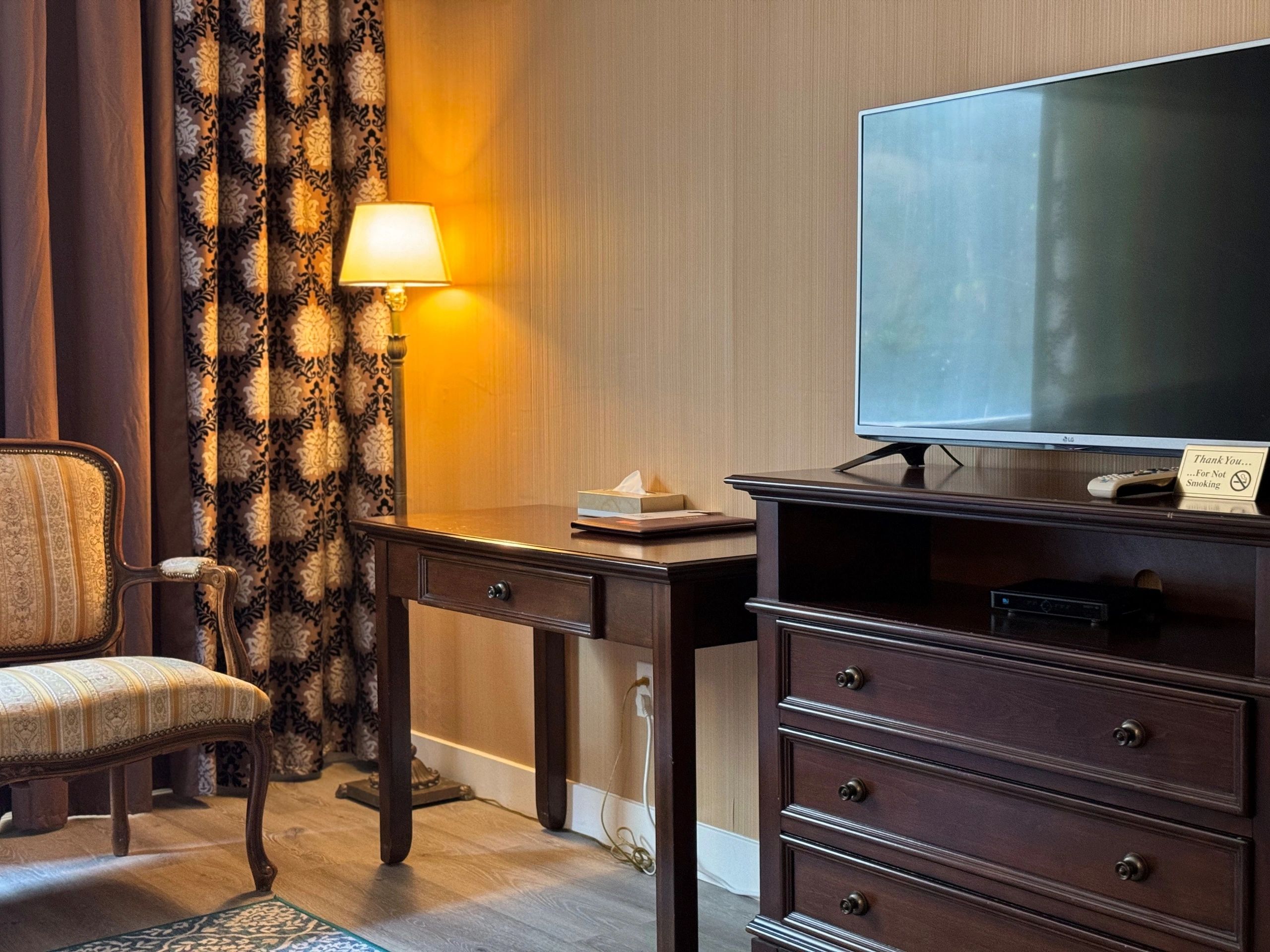 A hotel room with a chair, desk, TV, and dresser.