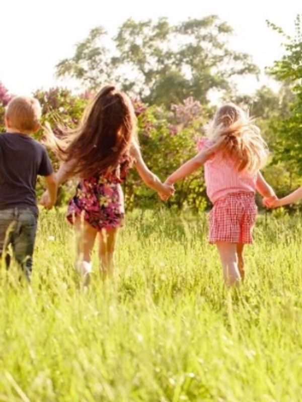 Children holding hands, running in a grassy field.