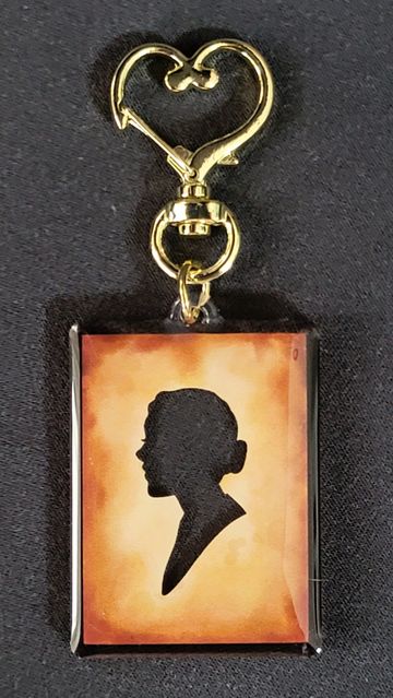 Gold heart-shaped keychain with a silhouette portrait on a rectangular pendant.