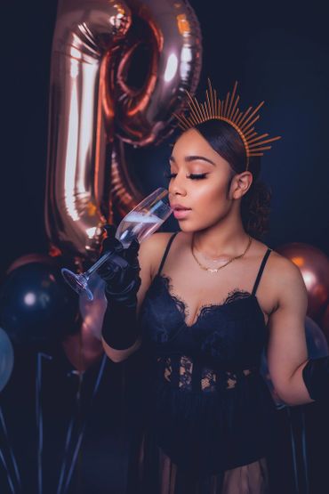 birthday photoshoot portrait with balloons, satin gloves, and crown drinking champagne