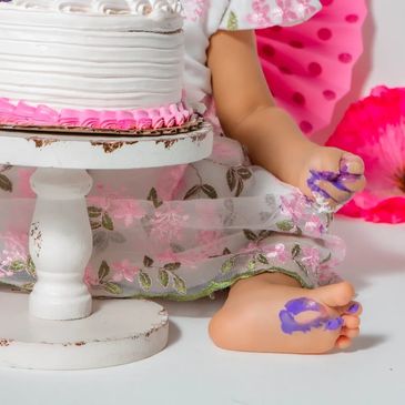 Child with colorful paint on hand and foot near a decorated cake.NYC Photography Pricing | Taisha Marie Photos